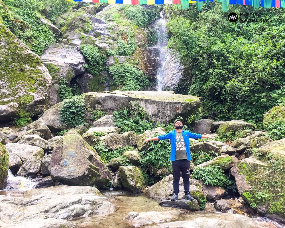 An asian man spreading his hands in front of the Lhasa Falls - Best Places to Visit in Gangtok